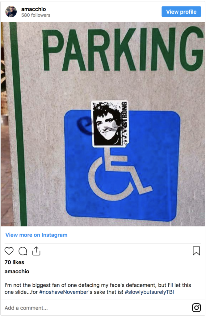 Picture of a handicap road sign with a black & white sticker of a male's face on it with vertical text that reads, "Stay Strong".
